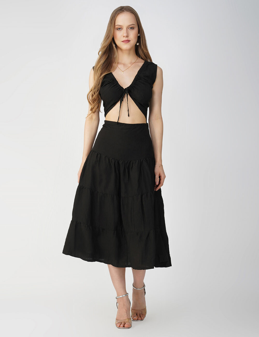 Model is wearing a sleeveless, flared long black dress made of soft cotton linen fabric, featuring a front tie detail. She is 5’8 in height and wearing size “M.”