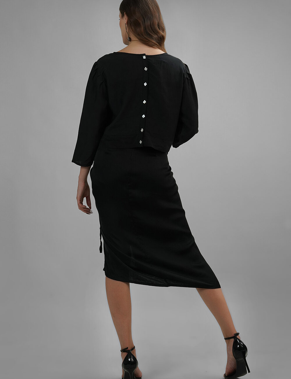 Model wearing black crop top with wide neckline and white diamond buttons on the back