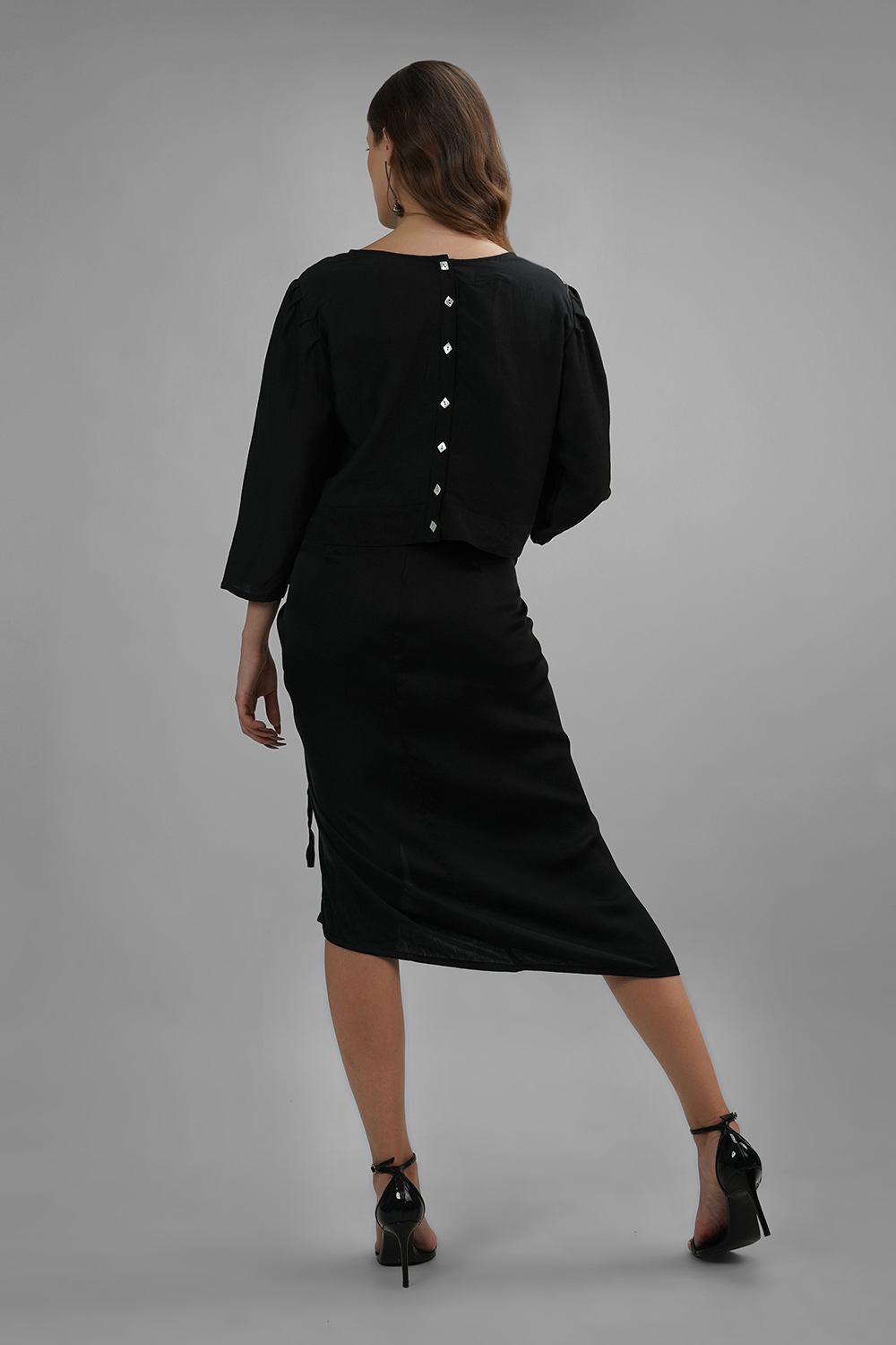 Model wearing black crop top with wide neckline and white diamond buttons on the back
