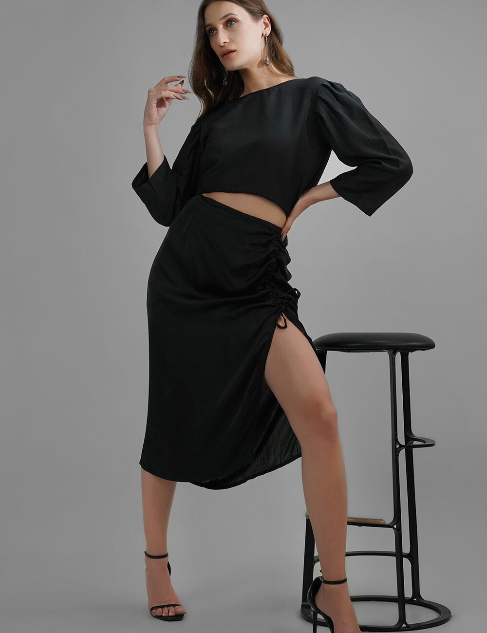 Model wearing black satin midi skirt with adjustable side slit and ruched detailing