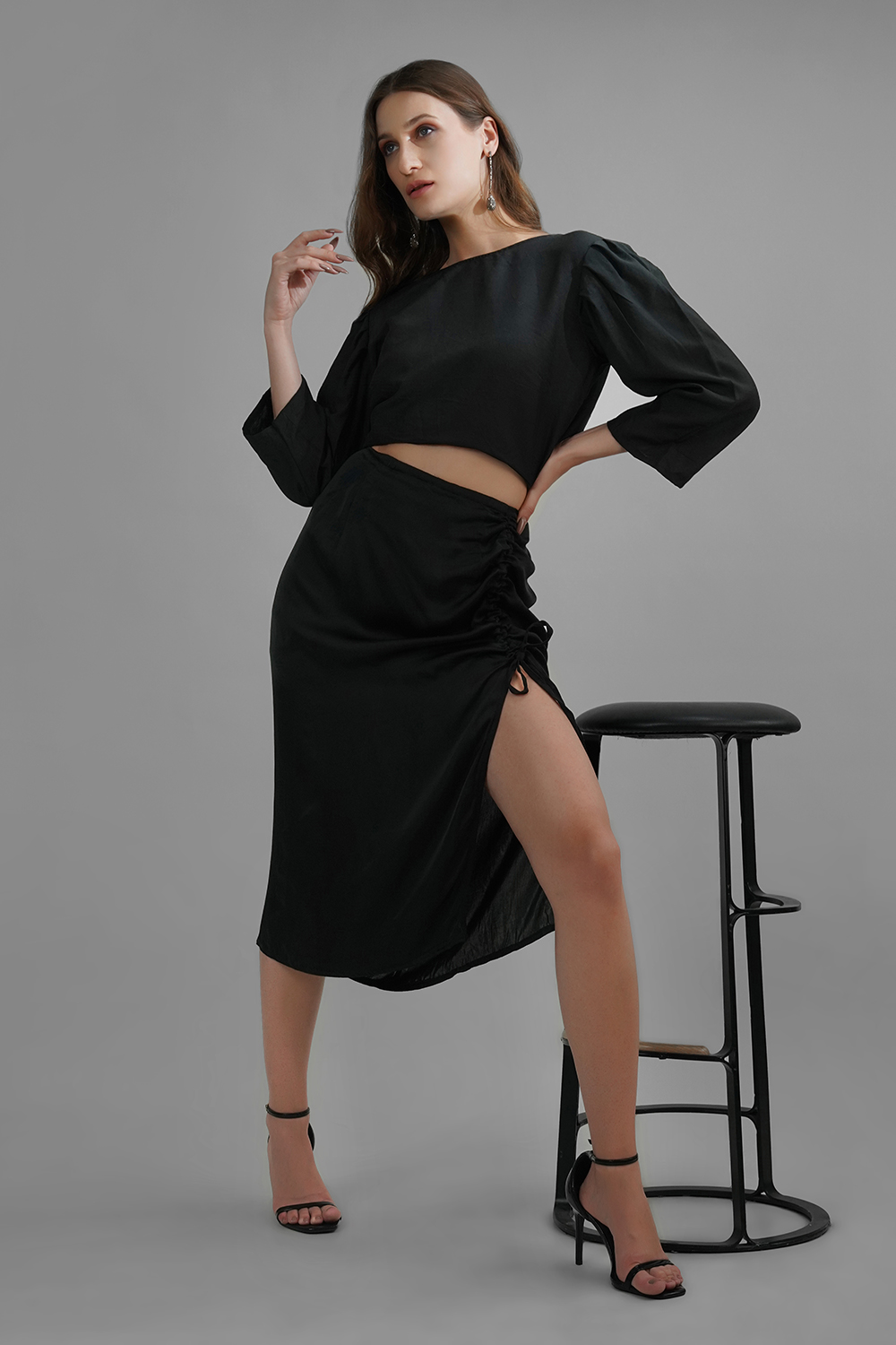 Model wearing black satin midi skirt with adjustable side slit and ruched detailing
